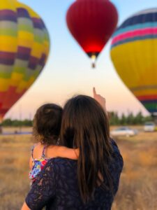 woman holding child pointing to hot air balloon